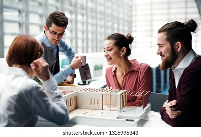 Group of young architects with model of a house working in office, talking.