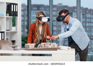 Group Of Young Architects At VR Goggles Working With Mock-up Of A House In Modern Office.