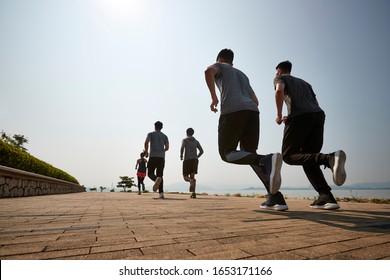 Group Of Young Asian Adult Men And Woman Running Outdoors, Rear And Low Angle View