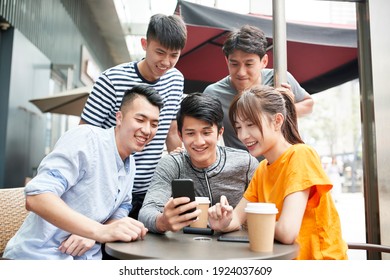 Group Of Young Asian Adults Four Men And And A Woman Looking At Mobile Phone Together Outdoors