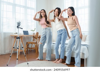 Group of young Asian Chinese female friends dancing in front of a mobile phone to share on social media application in bedroom. Cheerful Korean women influencer having live streaming on smartphone. - Powered by Shutterstock