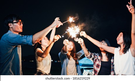 Group of young Asian college student friends lit light sparkler, sing and dance together at beach camping tent. Party people, love friendship relationship, or outdoor camping activity concept - Powered by Shutterstock