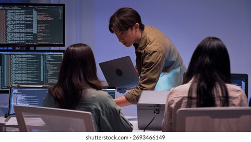 Group of young Asian developers collaborating during nighttime coding session. Team reviewing software issues and debugging source code in dark modern tech workspace. Innovation and teamwork in action