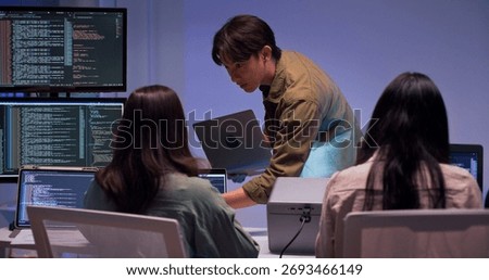 Group of young Asian developers collaborating during nighttime coding session. Team reviewing software issues and debugging source code in dark modern tech workspace. Innovation and teamwork in action