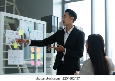 A Group Of Young Asian Entrepreneurs. Meeting To Review Stock Investment Data In A Meeting Room With Natural Light Windows.