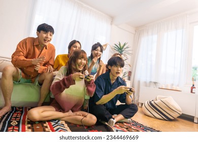 Group of Young Asian man and woman playing video games together in living room at home. Happy people friends enjoy and fun indoor activity lifestyle spending time together on holiday vacation. - Powered by Shutterstock