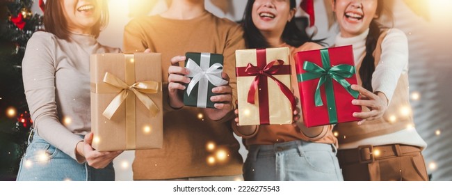 Group of young Asian man and women as friends having fun at a New Year's celebration, holding gift boxes standing by Christmas tree decoration, midnight countdown Party at home with holiday season. - Powered by Shutterstock