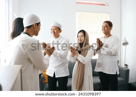 Group of young Asian muslim people forgiving each other by giving greet hands during Eid Mubarak celebration at home