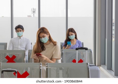 A group of young Asian passengers sit and wait in an airport terminal for their flight with masks on and keep social distance