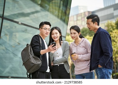 group of young asian people looking at cellphone together outdoors happy and smiling