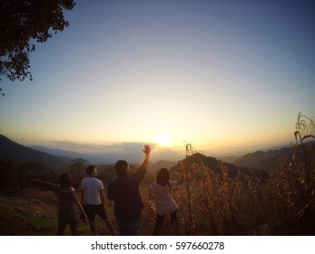 Group Of Young Asian People Stand On The Top Of Mountain, Wash Sunset And Hold The Hand Up To Say Goodbye The Sun. 