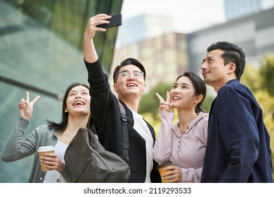group of young asian people taking a selfie using cellphone outdoors on street happy and smiling