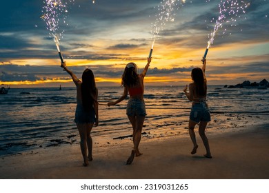 Group of Young Asian woman friends playing sparklers firework together at tropical island beach in summer night. Attractive girl enjoy and fun outdoor lifestyle beach party on holiday travel vacation.