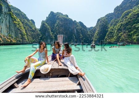 Group of Young Asian woman friends sitting on the boat passing island beach lagoon in summer sunny day. Attractive girl enjoy and fun outdoor lifestyle travel on summer holiday vacation in Thailand
