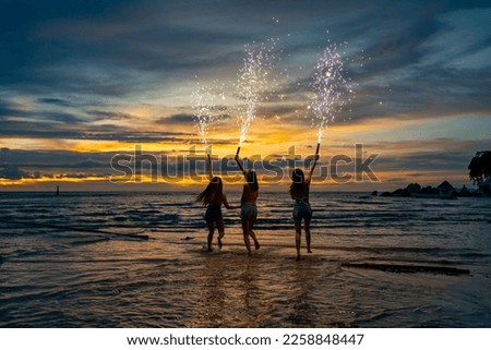 Group of Young Asian woman friends dancing and playing sparklers firework together at tropical beach in summer night. Happy girl enjoy and fun outdoor lifestyle nightlife party on holiday vacation.