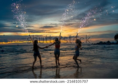 Group of Young Asian woman having fun dancing and playing sparklers together on tropical beach in summer night. Happy female friends enjoy outdoor lifestyle nightlife on holiday travel vacation trip