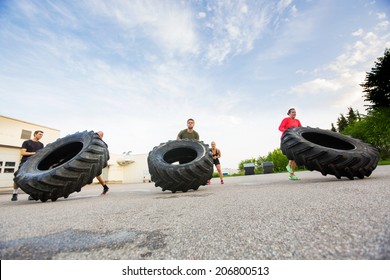 Group of young athletes doing tire-flip exercise outdoors - Powered by Shutterstock