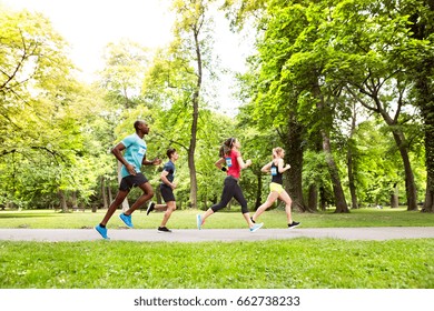 Group Of Young Athletes Running In Green Sunny Park.