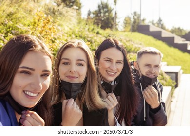 Group of young and attractive friends taking selfie with taking off black medicine faces masks during coronavirus outbreak. Bright vivid backlight filter. Second from left woman is in camera focus