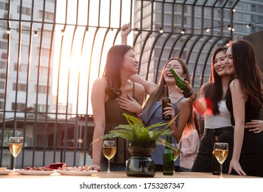 Group Of Young Beautiful Asian Friends Are Dancing Together Feeling Happy And Funny And Holding Beer Bottle In Party At Rooftop On Evening .