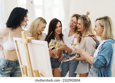 Group of young beautiful women paint on canvas and drinking white wine during party at home