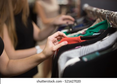 Group of young beautiful women shopping in fashion mall, choosing new clothes, looking through hangers with different casual colorful garments on hangers, close up of hands/ Shopping concept - Powered by Shutterstock - Get 15% off with code: PIKWIZARD15