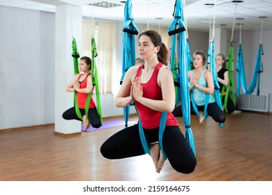 Group of young beautiful yogi women doing aerial yoga practice in hammocks in fitness club.