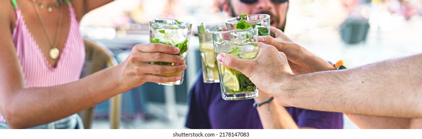 Group of young best friends clinking with long drink booze glasses and having a celebratory toast together in the bar by the sea - people, joyful living and carefree people lifestyle concept