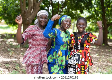 Group of young black African villagers in colourful traditional dresses smiling at the camera with their clenched fists as a symbol for women's strength and gender equality