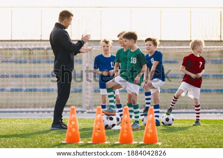Group of young boys on football training. Kids practicing soccer on grass field. Young man as a soccer coach explaing to players training rules. Children exercising with soccer balls
