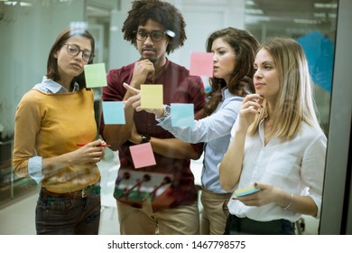 Group of young business people discussing in front of glass wall using post it notes and stickers at startup office - Powered by Shutterstock