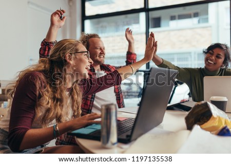 Group of young business team giving high five and celebrating success at office. Cheerful startup business team rejoicing success at office.