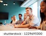 Group Of Young Candidates Sitting At Boardroom Table Listening To Presentation At Business Graduate Recruitment Assessment Day