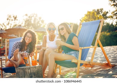 Group Of Young Casual Female Friends Sitting On Beach On Sun Beds,hangout And Relaxing.