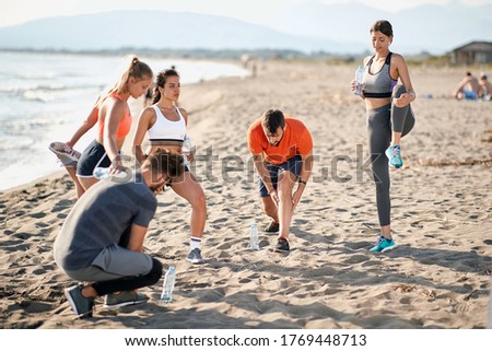 group of young caucasian men and women stretching, warming up for exercising at the beach