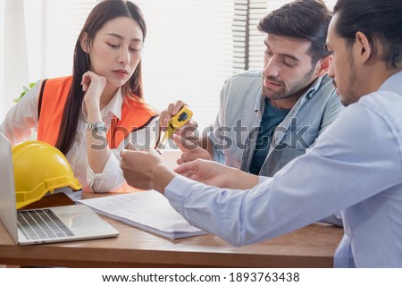 Group of young caucasian,asian colleagues or contractors, engineer brainstorming, discussing and talking to plan while looking at tape measure on the table at workplace, office.Working people concept.