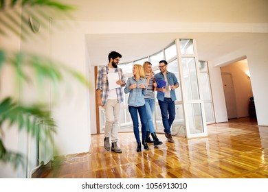 A Group Of Young Cheerful Business People Walking Down The Bright Hallway While Discussing And Drinking Coffee From Cups. 