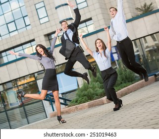 Group Of Young Cheerful Business People In Front Of Office Building, Photographed At The Moment Of The Jump.