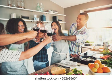 Group of young cheerful friends cheering with wine glasses while cooking some tasteful food at kitchen. - Powered by Shutterstock