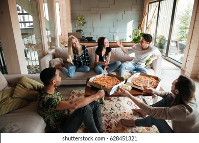 Group of young cheerful friends hanging out together at home with pizza and beer