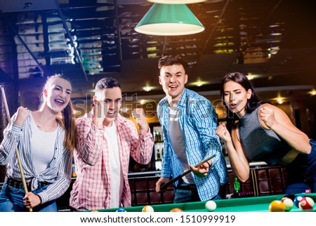Group of young cheerful friends playing billiards. Funny time after work