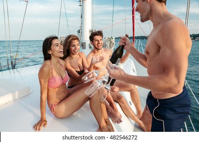 Group of young cheerful happy friends having fun on the yacht and drinking champagne