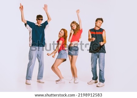 Group of young, cheerful, stylish people dancing isolated over grey background. Disco, party. Jeans fashion. Boys and girls having fun. Concept of youth, retro style, 90s era, fashion, lifestyle, ad