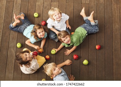 A group of young children seated on wooden decking surrounded by a selection of apples