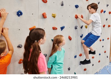 A group of young children stand together in front of a climbing wall, listening attentively to their teachers instructions before attempting to scale the wall. - Powered by Shutterstock