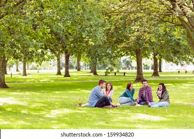 Group Of Young College Students Sitting On Grass In The Park