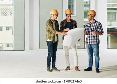 Group Of Young Contractors In Hardhats Discussing Contruction Plan At Meeting And Planning Work