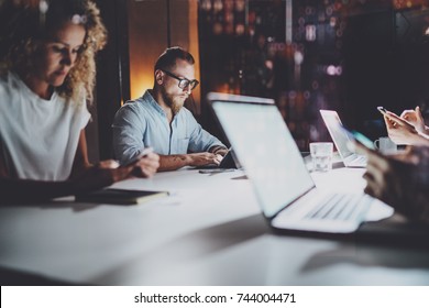 Group Of Young Coworkers Work Together At Night Modern Business Office.Young People Using Electronic Laptops At The Table.Horizontal.Blurred Background