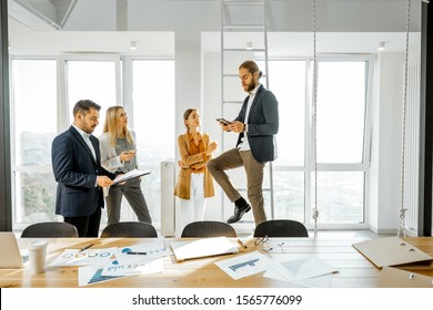 Group Of A Young Creative Office Employees Having Some Informal Discussion, While Standing Together In The Bright Meeting Room With Large Windows