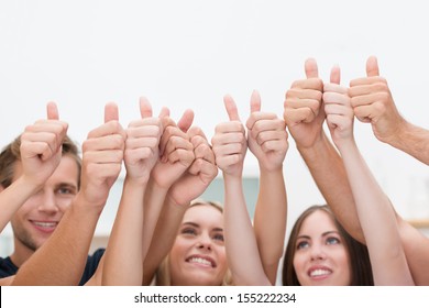 Group Of Young Diverse Business People Giving A Thumbs Up Standing With Their Arms Raised In The Air To Indicate Their Success And Approval